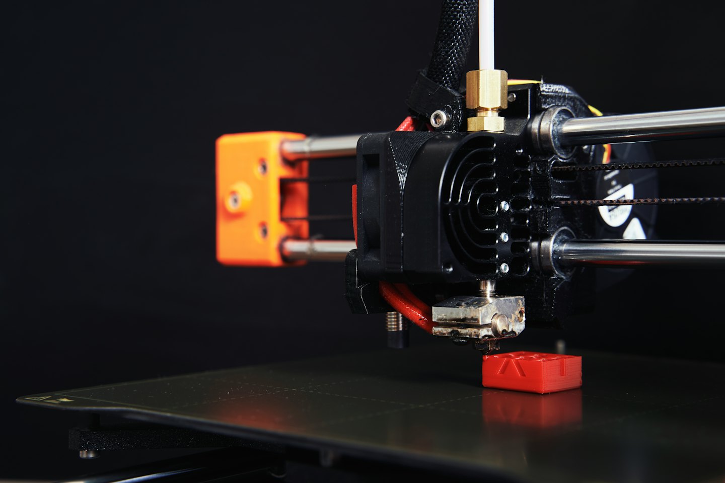 Drukarka 3D budująca mały czerwony przedmiot.