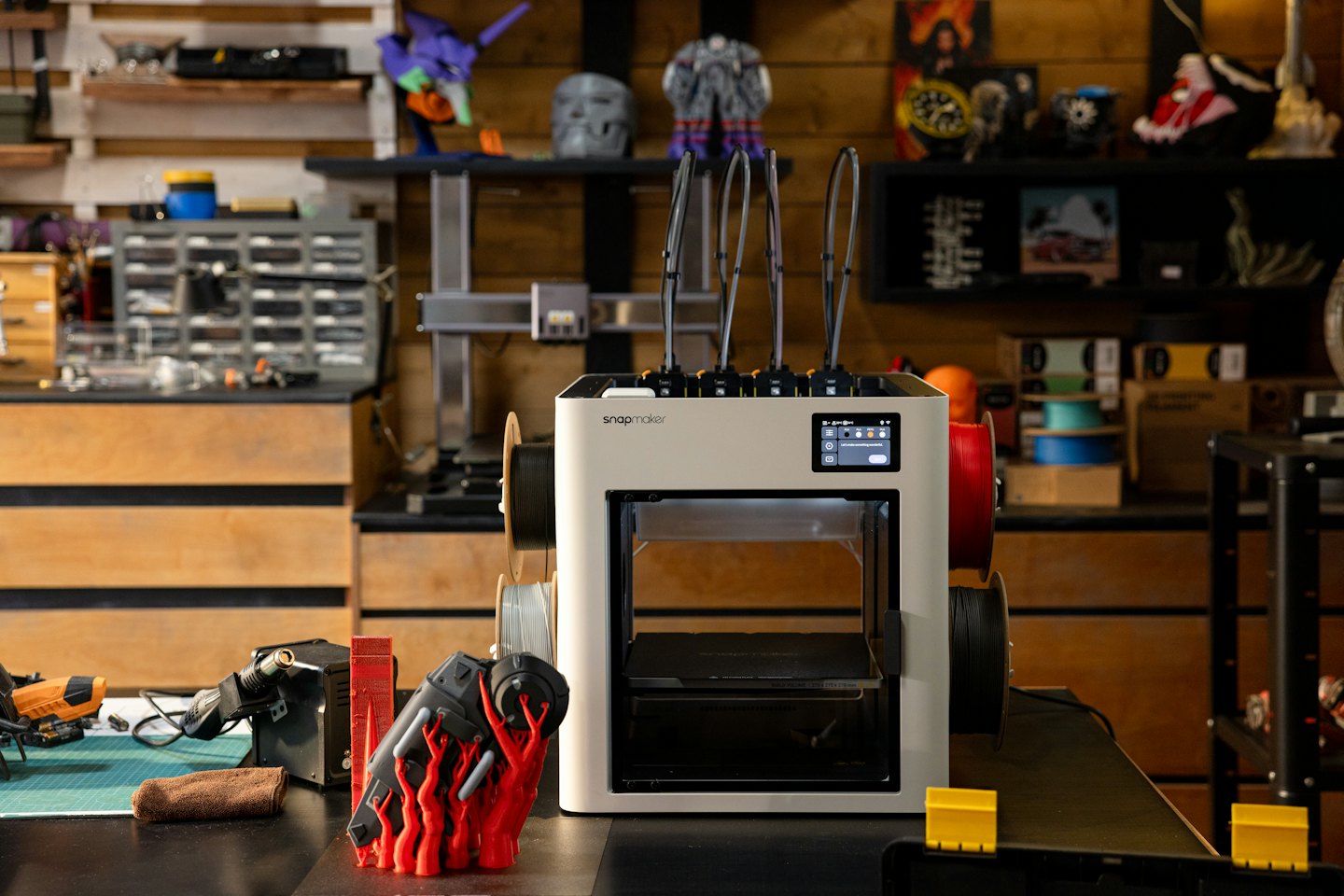 Drukarka 3D Snapmaker na stole warsztatowym z narzędziami i materiałami.